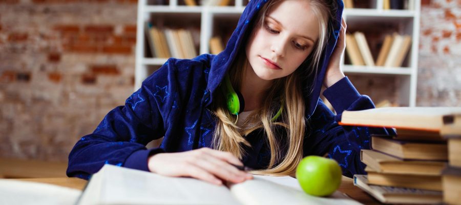 pexels-photo-1326947-1326947 Teenage girl in blue hood reads in library, headphones and apple by her side.