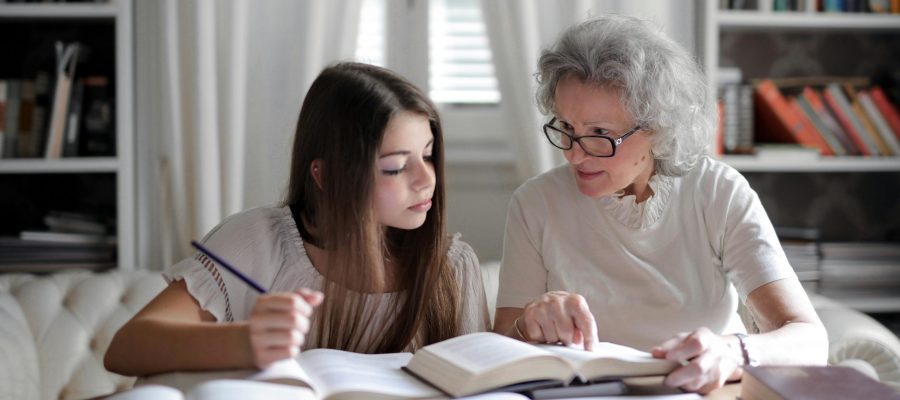 pexels-photo-3768129-3768129 A grandmother helps her teenage granddaughter with homework, surrounded by books indoors.
